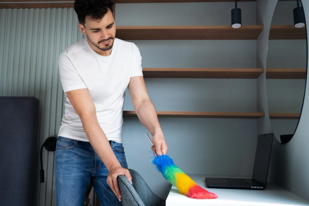 Reinigungskraft staubt einen Schreibtisch in einem hellen Wohnraum ab